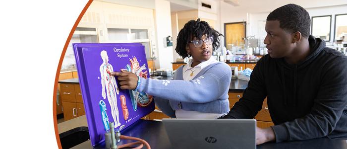 Two students working a science lab looking at a circulatory system book.