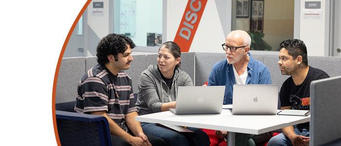 Four people sitting at a table working on two computers together.